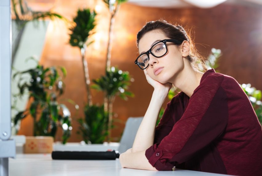 Unhappy beautiful young business woman in glasses sitting in office