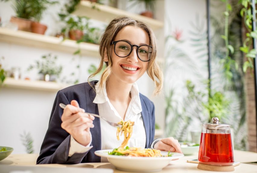 Businesswoman having lunch with pasta and fruit tea at the vegan restaurant on the green background